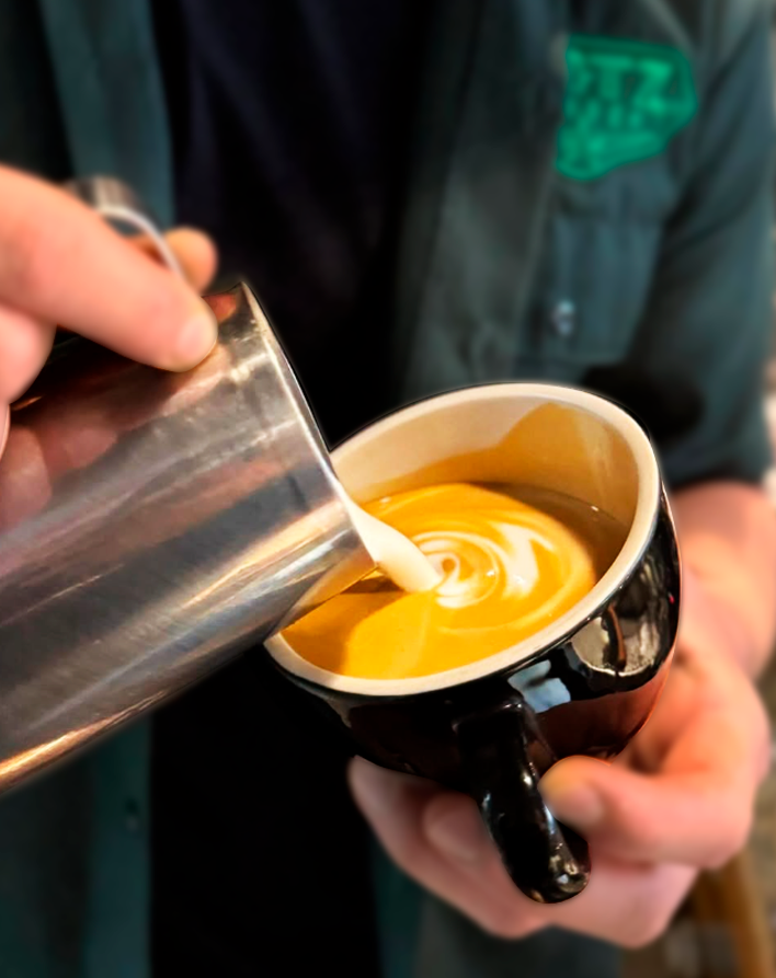 Barista sirviendo leche texturizada sobre un latte